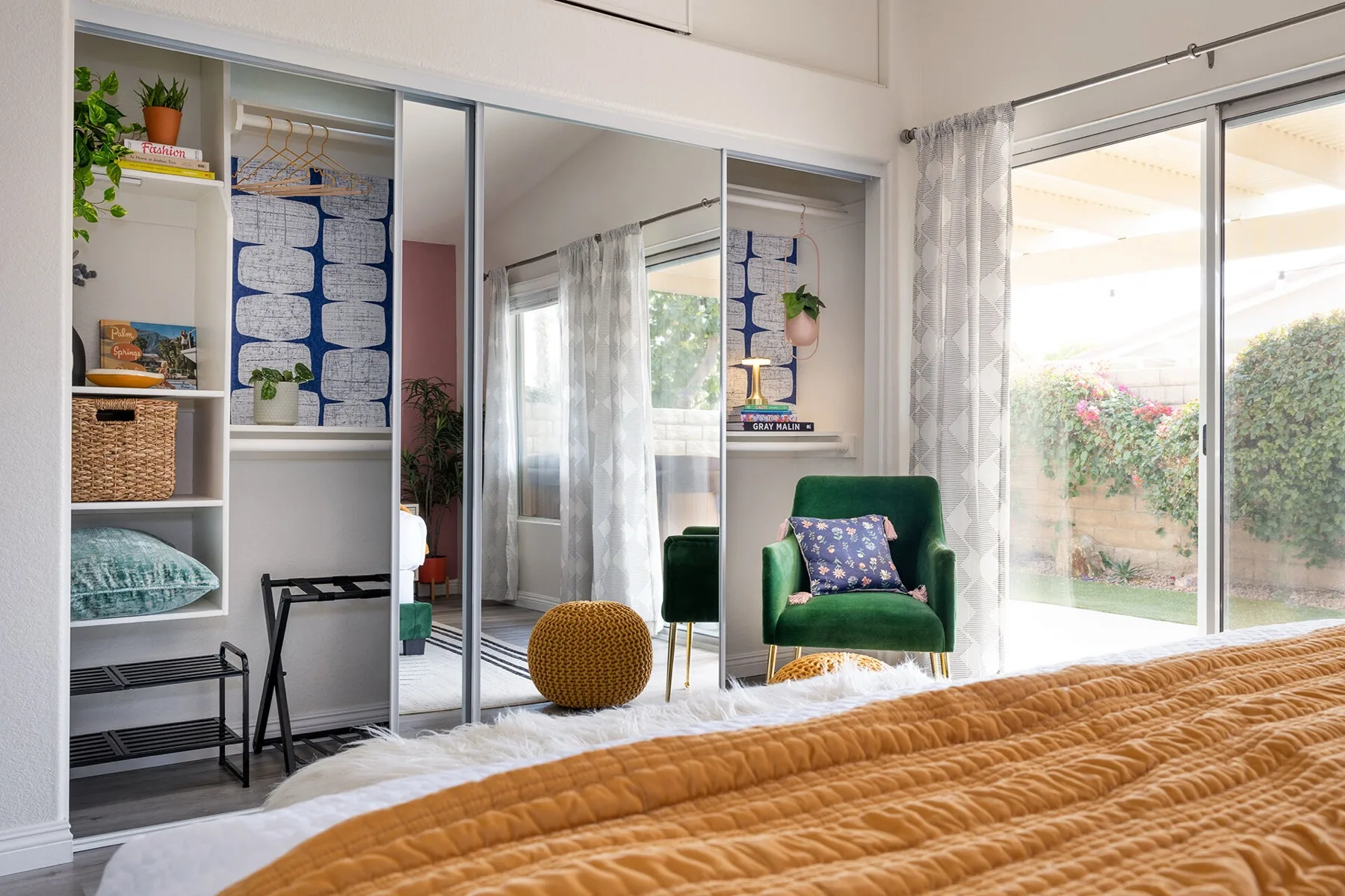 The Cozy Cactus bedroom after renovation with navy geometric wallpaper closet, emerald green velvet chair, and mustard pouf