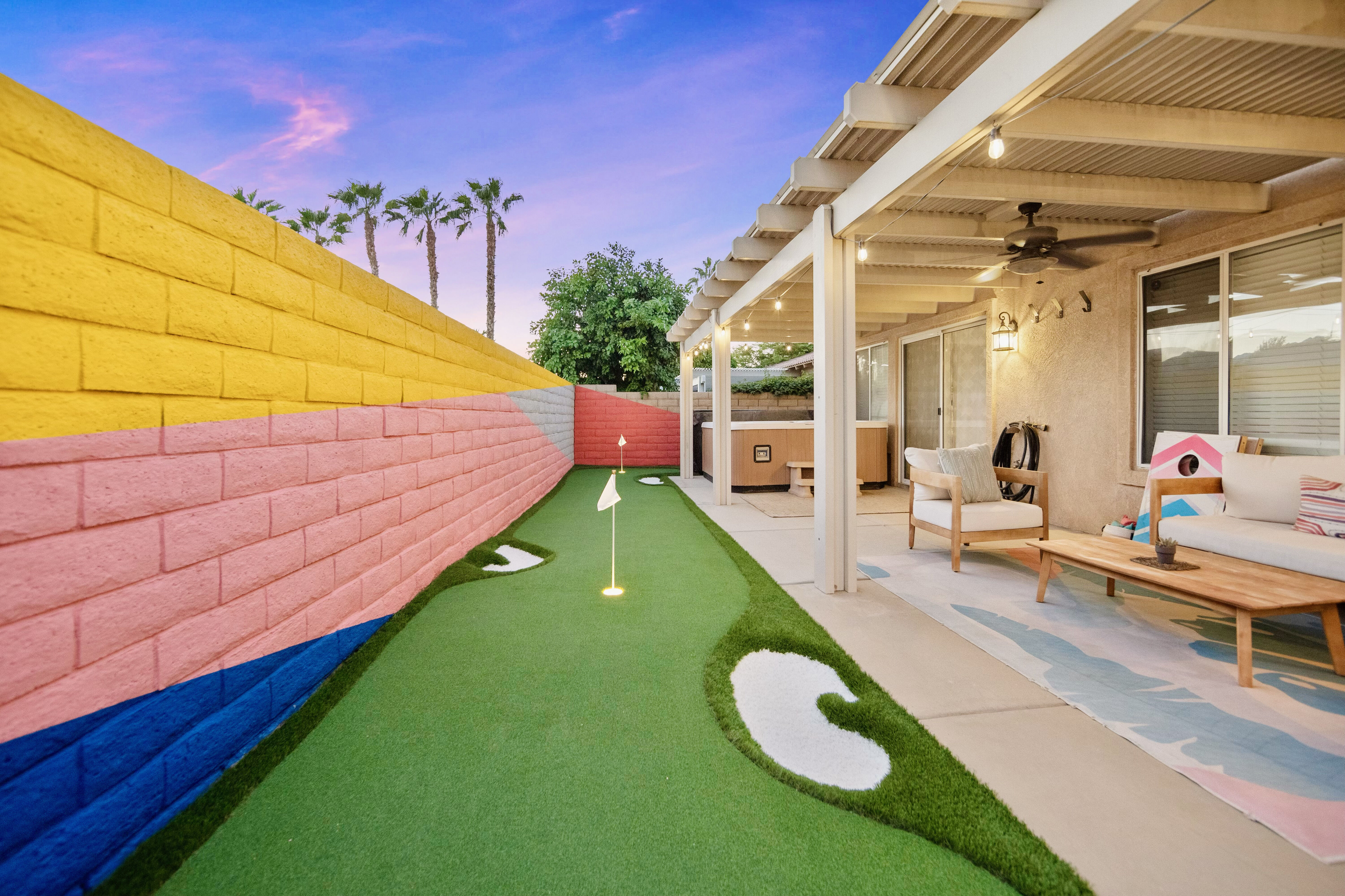 Backyard at the Cozy Cactus vacation rental in Indio California with putting green, covered patio, outdoor seating, and private hot tub at sunset