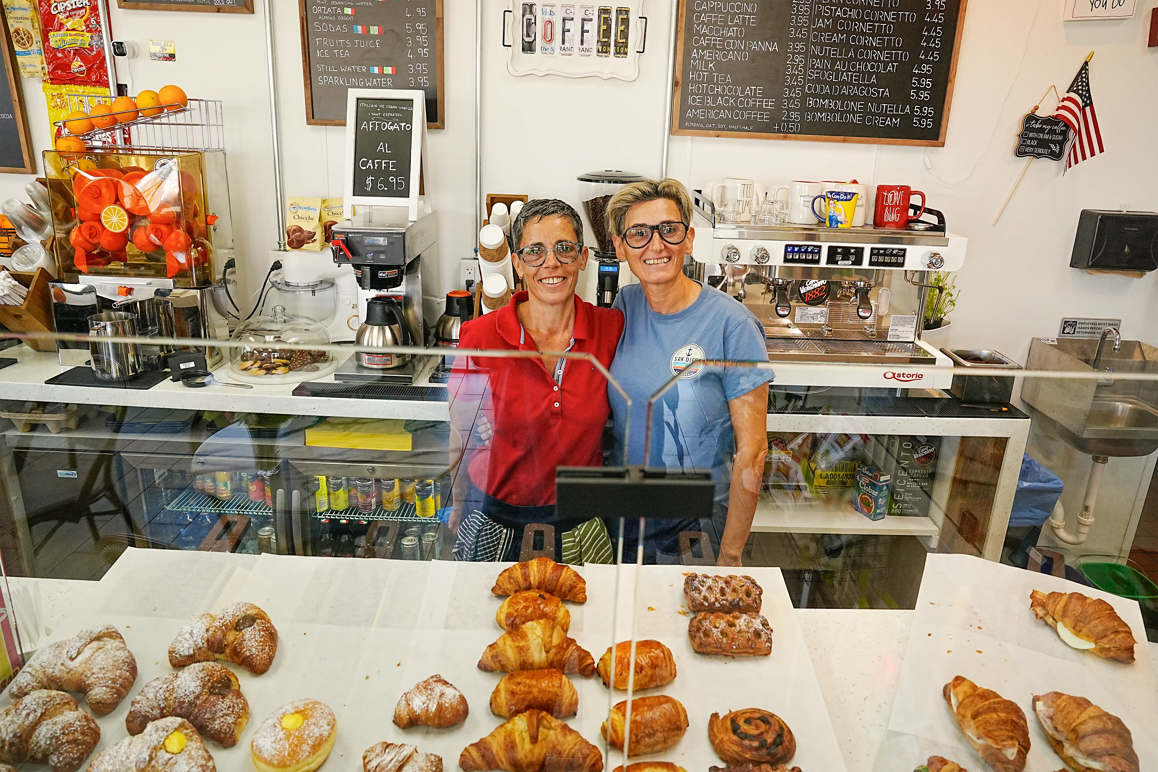 Owners of Les Filles Cafe standing behind the pastry counter in Cathedral City with croissants and French pastries in the foreground