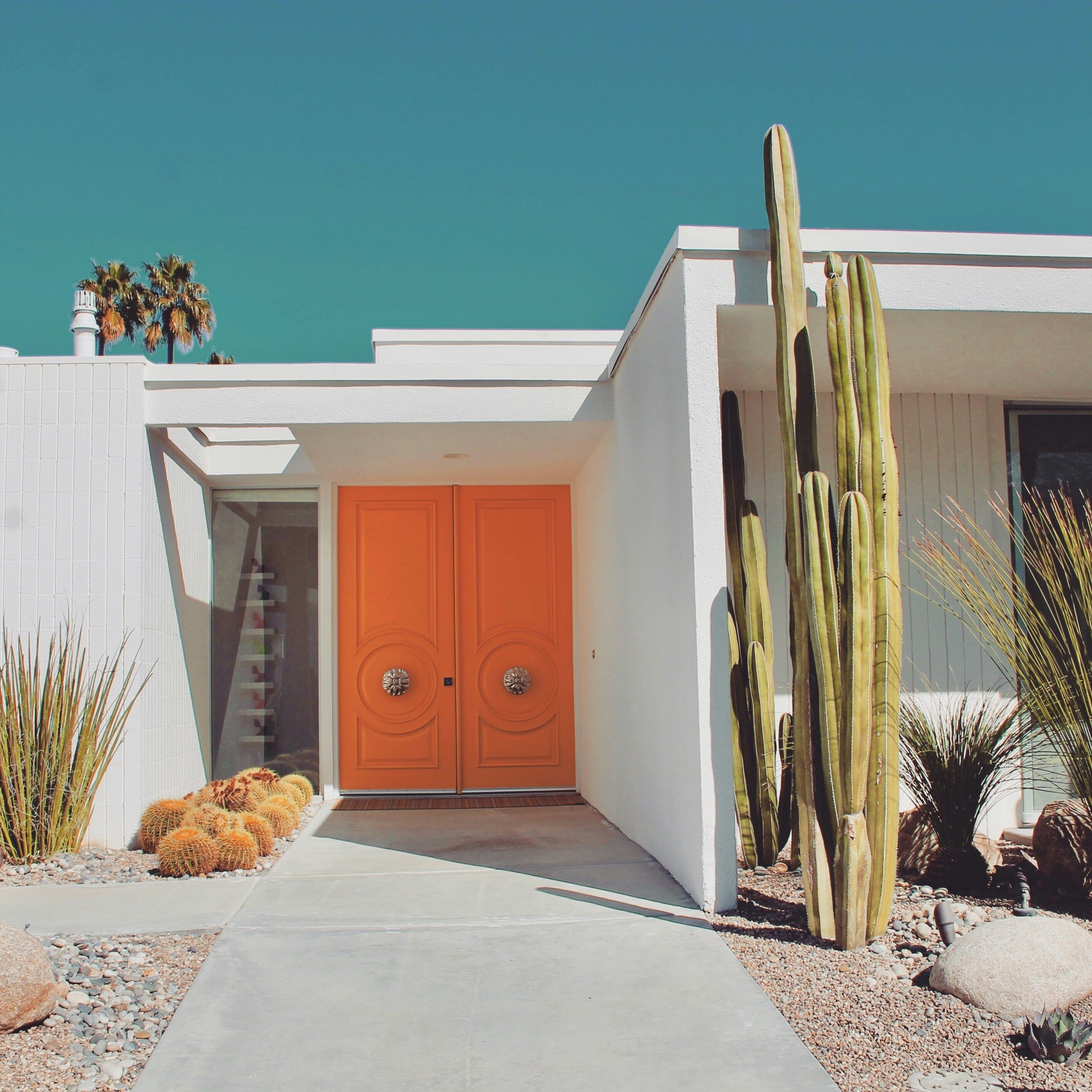 Vibrant orange front door of a midcentury modern home in Palm Springs with desert garden and blue sky