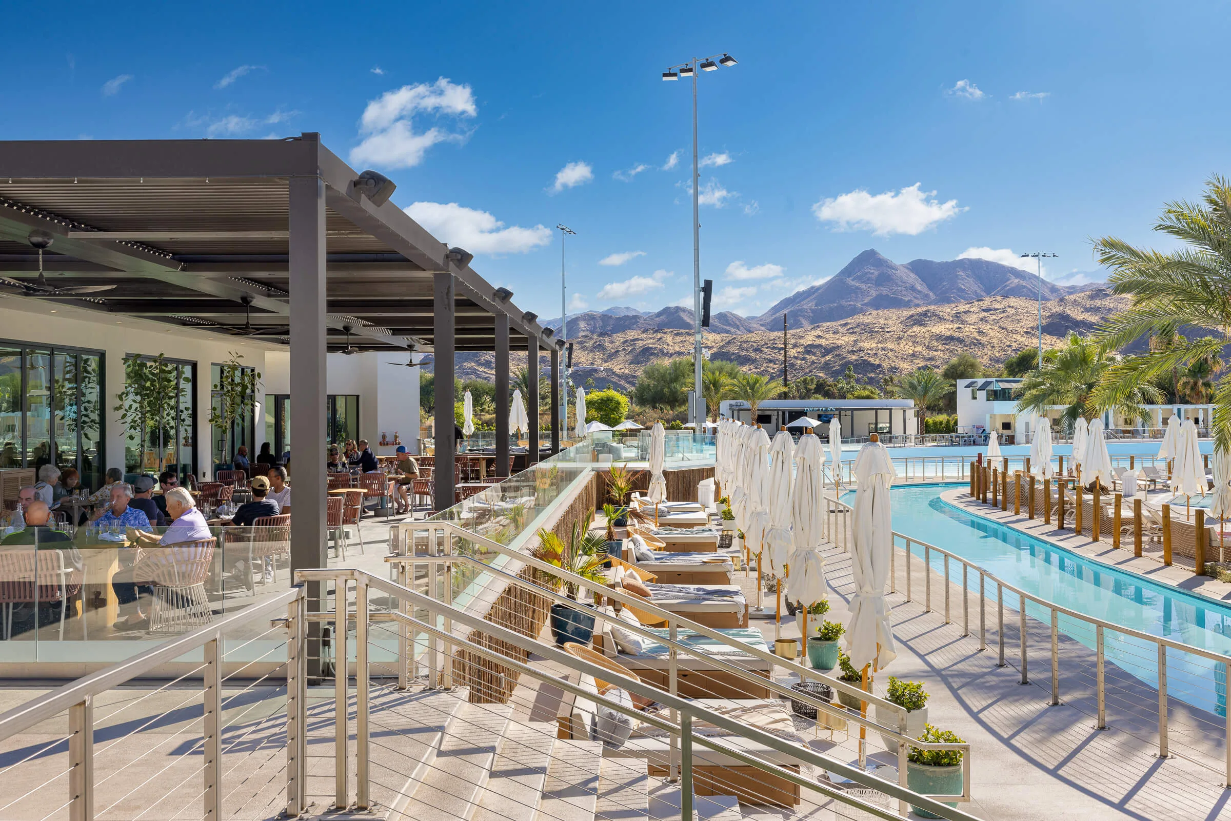 PSSC restaurant terrace with diners overlooking the wave pool lounge and desert mountains at Palm Springs Surf Club