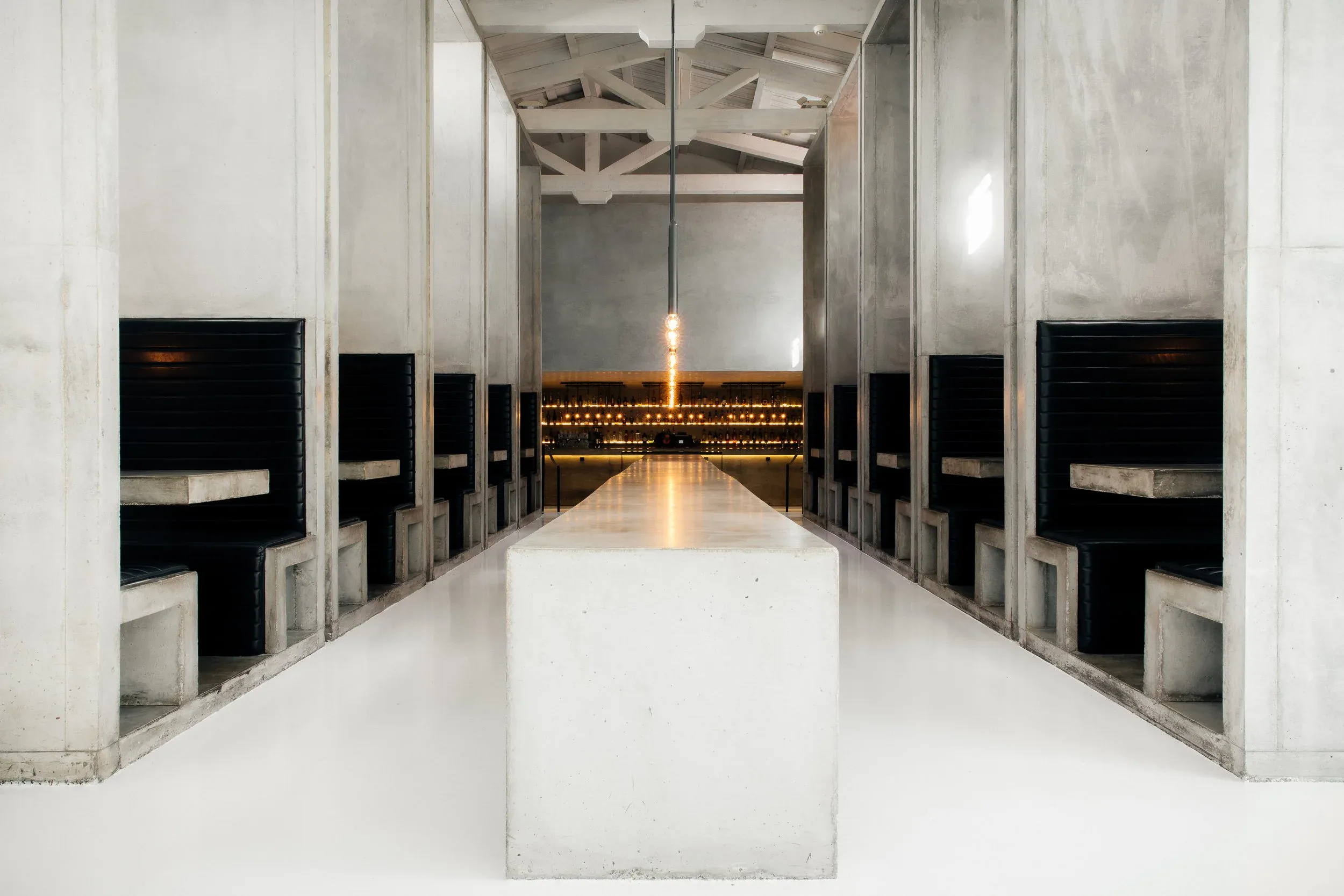 Workshop Kitchen and Bar interior in Palm Springs showing high concrete ceilings, long communal table, and dramatic bar at the end of the room