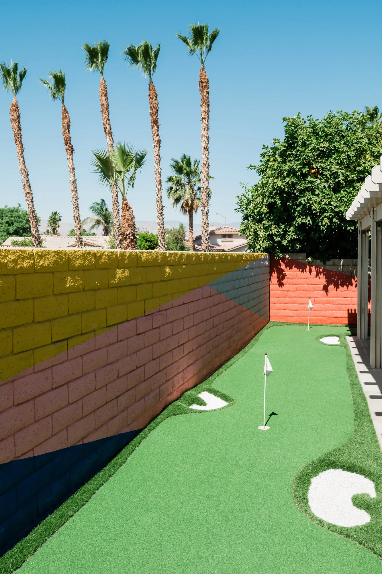 Cozy Cactus putting green with colorful painted block wall and palm trees in background