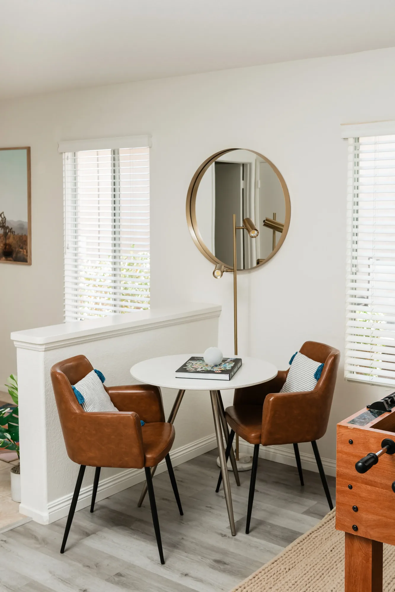 Cozy Cactus dining area with round white table, tan leather chairs, gold round mirror, and foosball table
