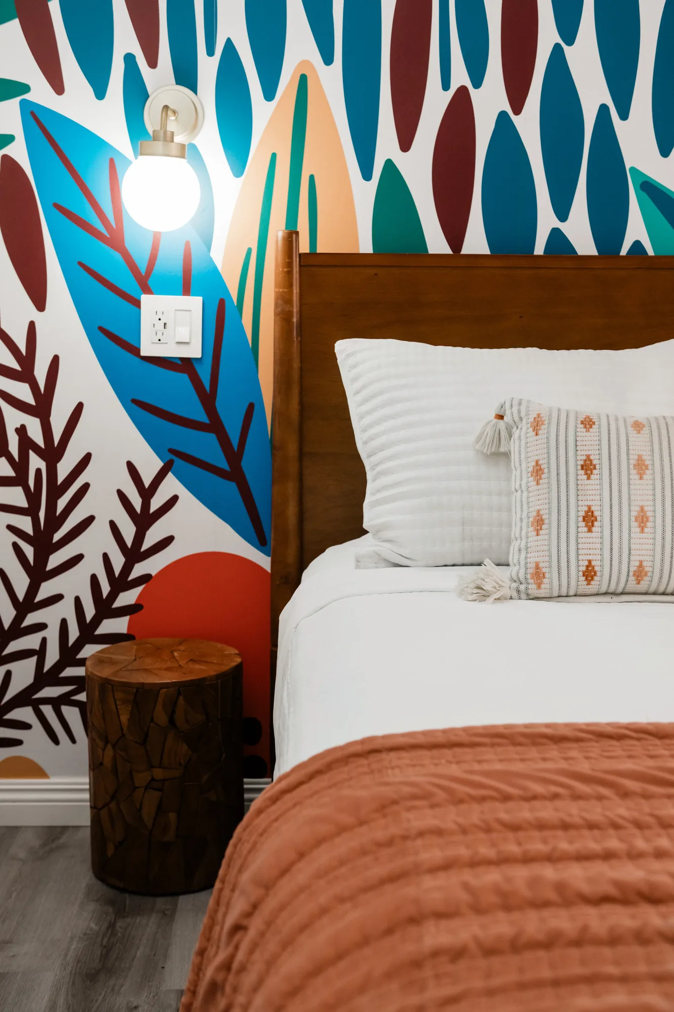 Cozy Cactus second bedroom with floor-to-ceiling surfboard botanical mural, wooden queen headboard, and terracotta bedding