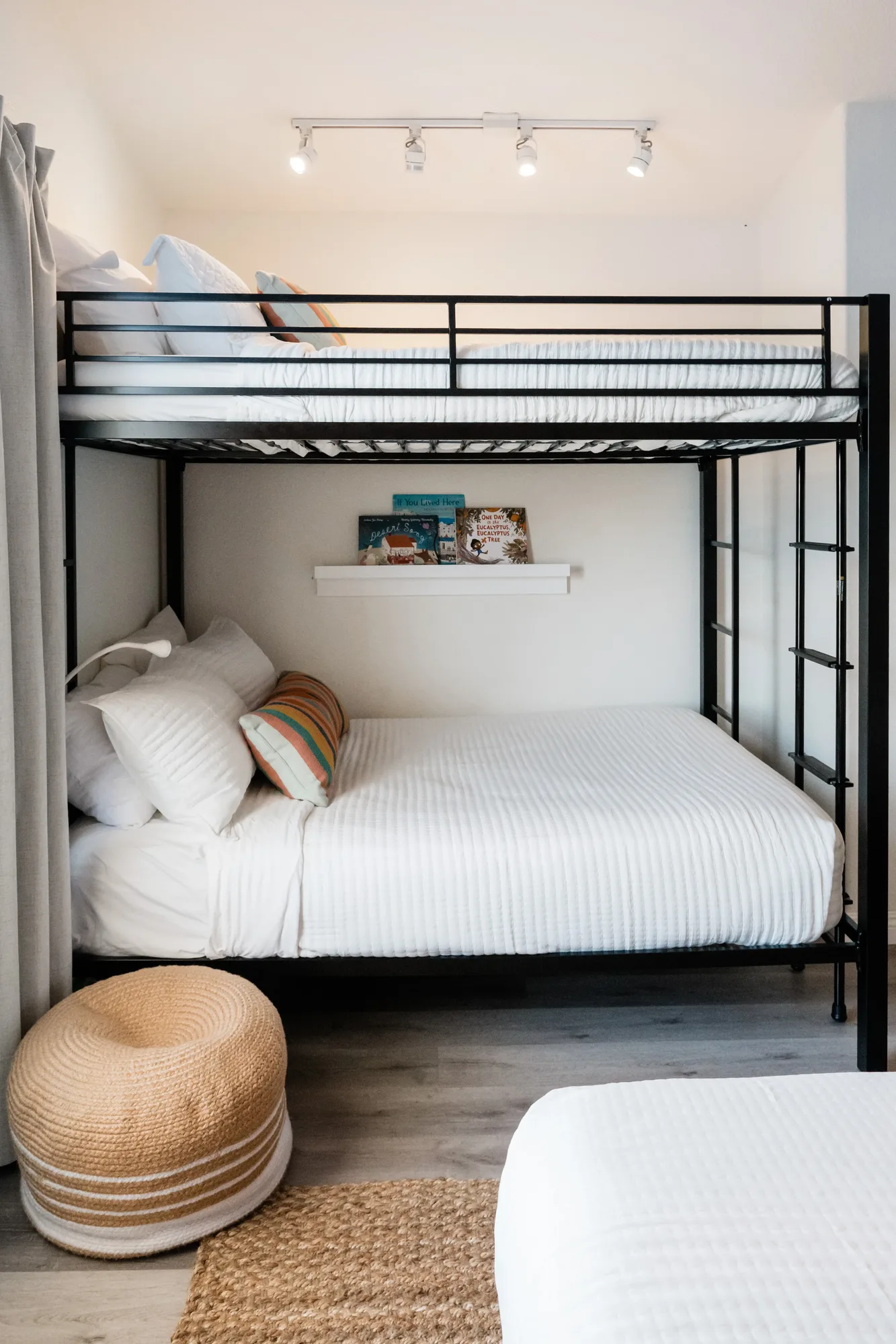 Cozy Cactus black metal bunk beds with white bedding, book ledge, and rattan pouf