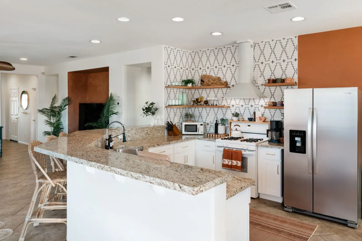 Terra Luz kitchen island with three rattan bar stools, stainless fridge, open shelves, and terracotta accent wall