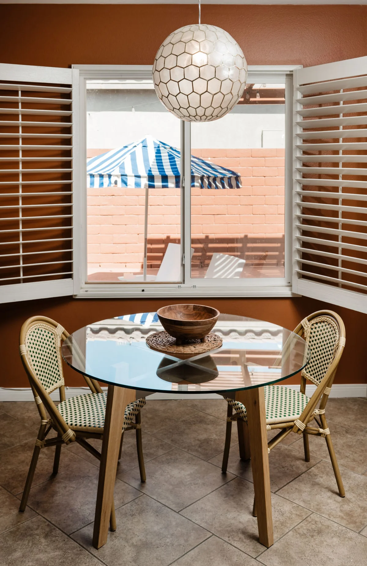 Terra Luz breakfast nook with open plantation shutters looking out to backyard blue striped umbrella and pool