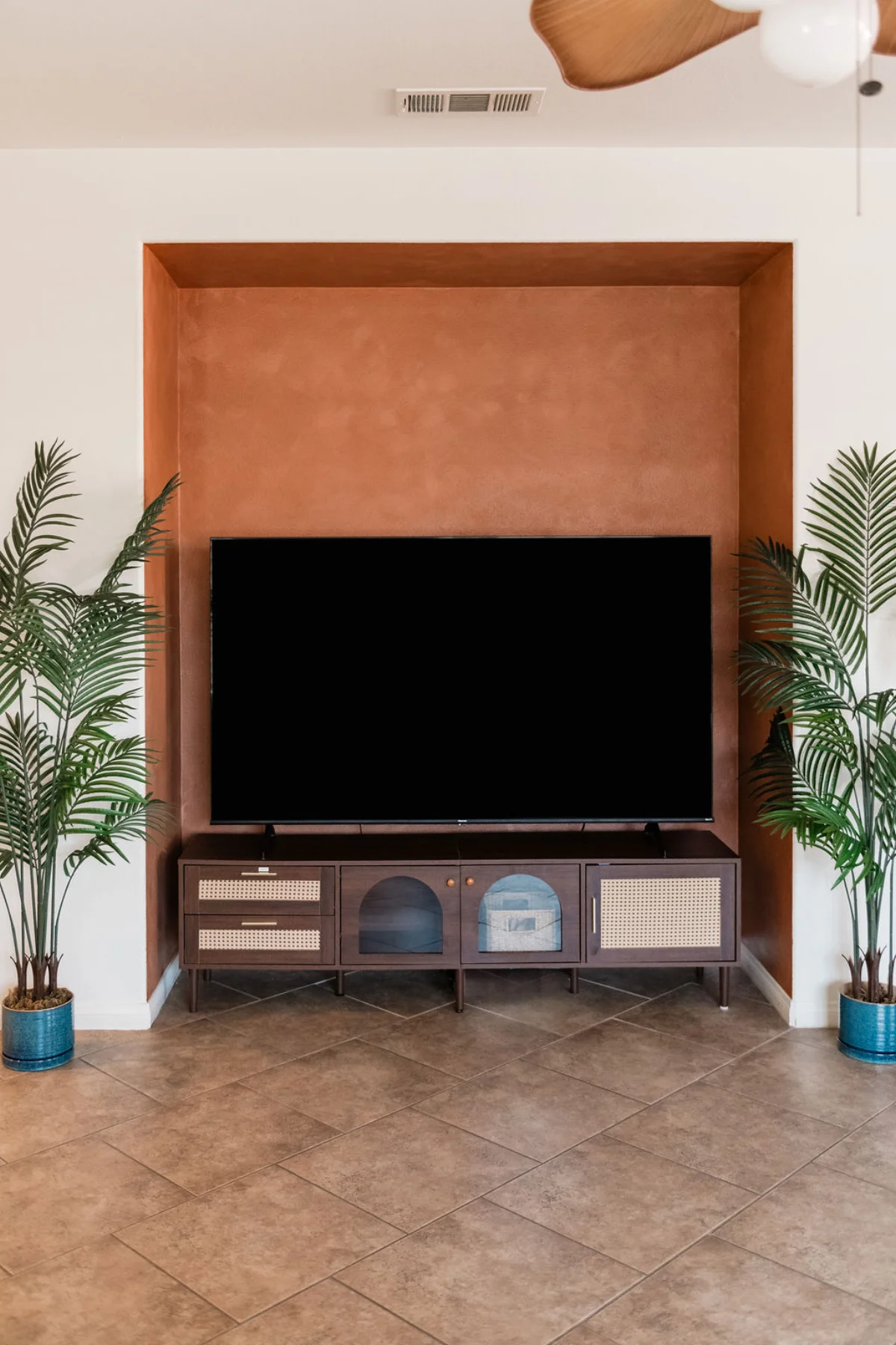 Terra Luz living room terracotta lime-wash TV niche with walnut rattan credenza and two fan palms in blue pots