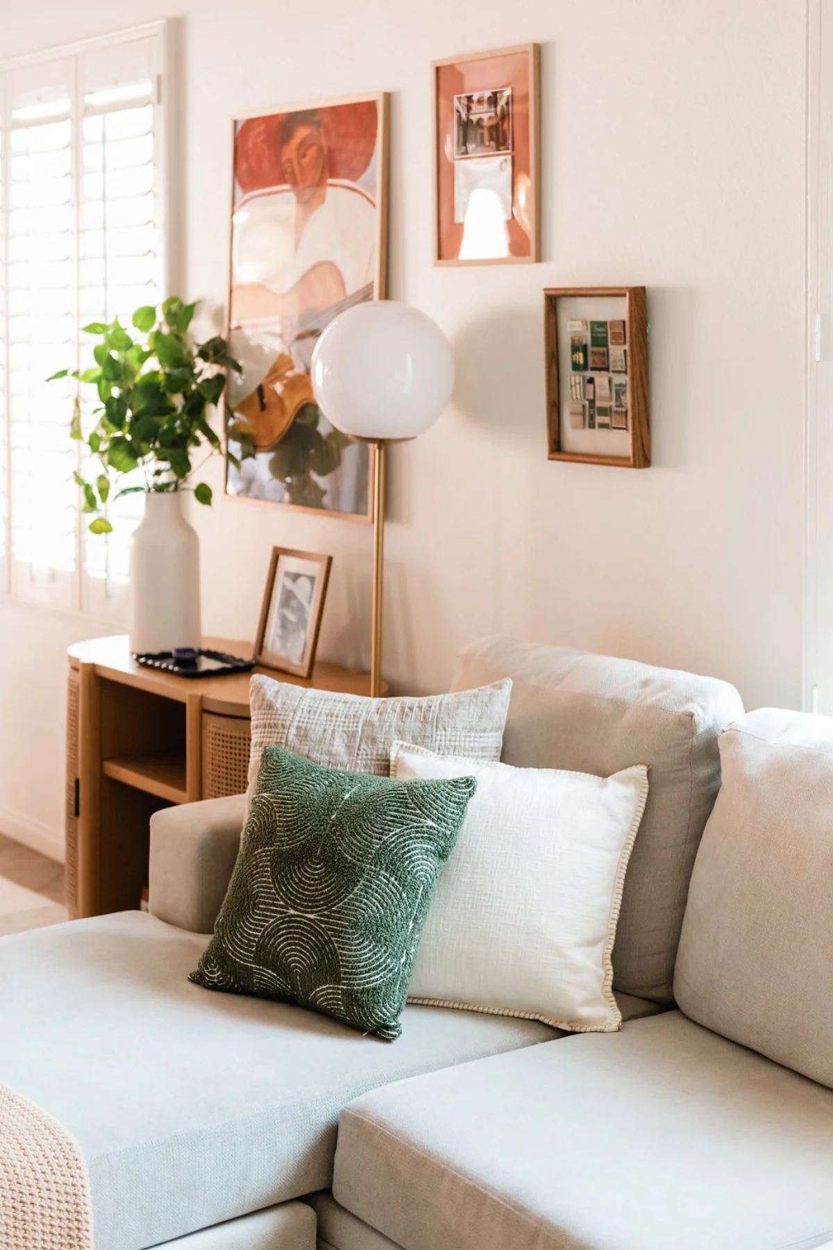 Terra Luz living room sofa with green beaded pillow, linen pillow, globe floor lamp, and rattan console with framed art gallery wall