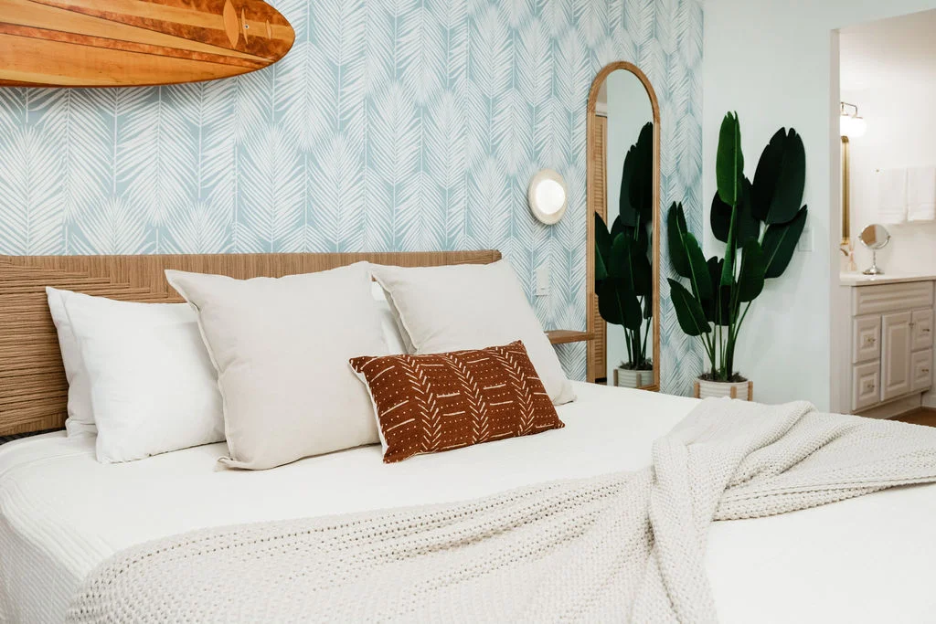 The Sundune Palm Springs primary bedroom with blue leaf wallpaper, rattan headboard, surfboard, and oval mirror