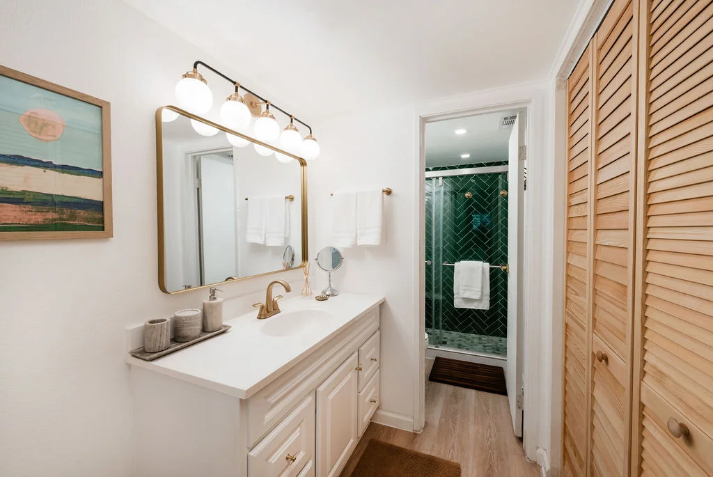 The Sundune Palm Springs second bathroom with white vanity, gold fixtures, and green herringbone tile shower