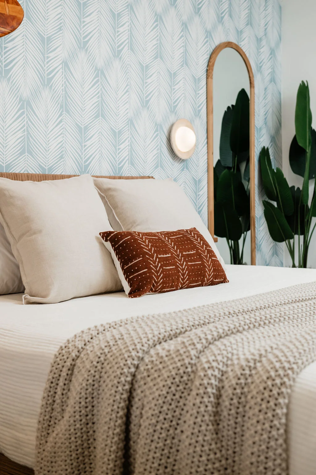 The Sundune Palm Springs primary bedroom king bed close-up with blue leaf wallpaper and rust throw pillow