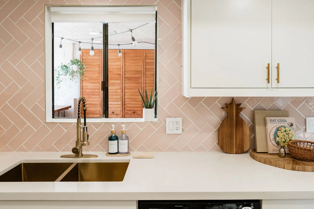 The Sundune Palm Springs kitchen with pink herringbone tile backsplash, gold sink, and white cabinets
