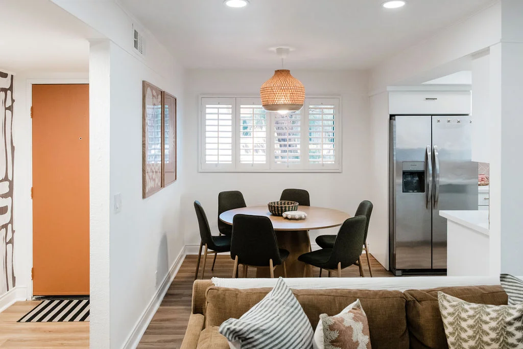 The Sundune Palm Springs dining area with round walnut table, black chairs, and wicker pendant